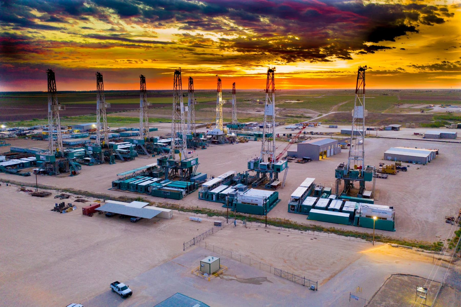 Multiple drilling rigs at a West Texas yard beneath a dramatic sunset