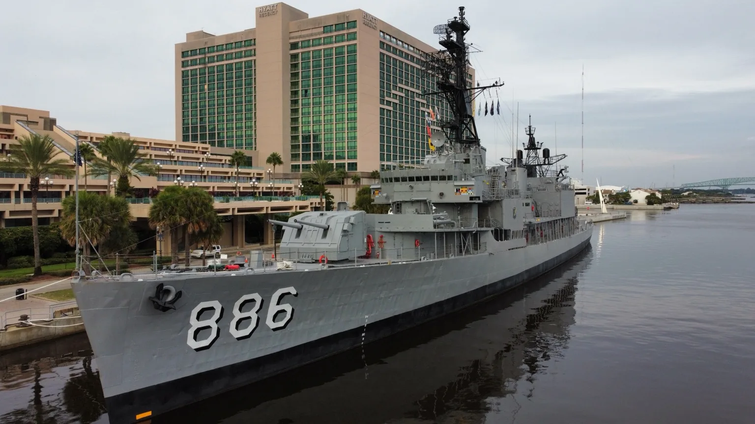 Aerial photo of a naval ship docked beside a waterfront hotel